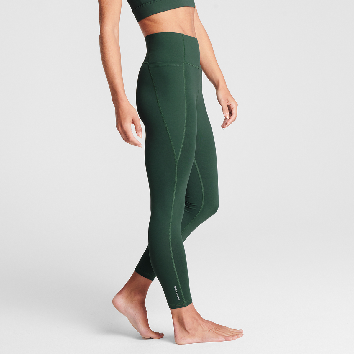 Woman wearing olive Trimline 7/8 Leggings by Definite Articles, side view.