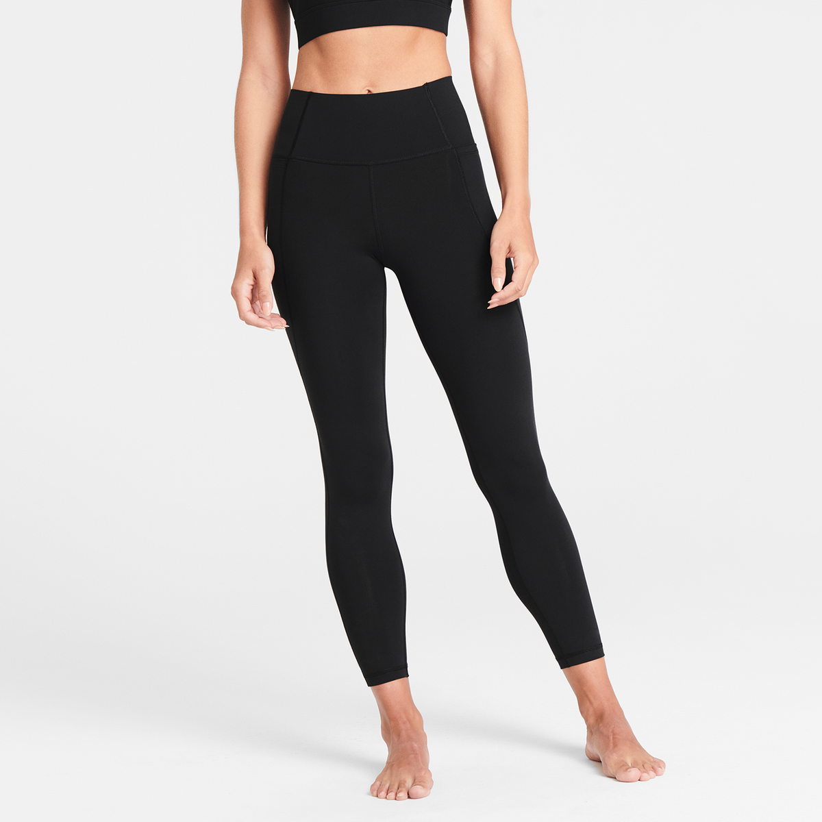 Woman wearing black Trimline Natural-Waist 7/8 Leggings by Definite Articles, white background.